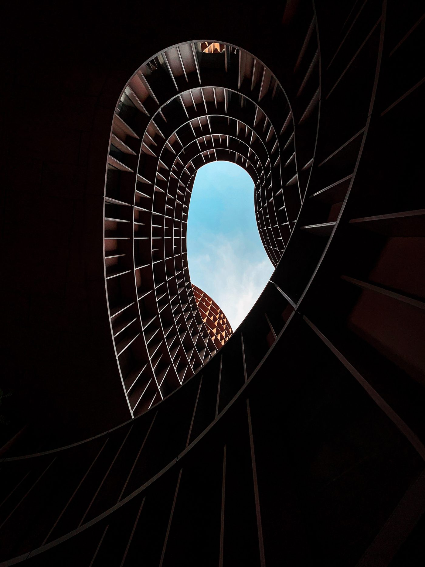 Looking up through a spiral staircase toward the sky